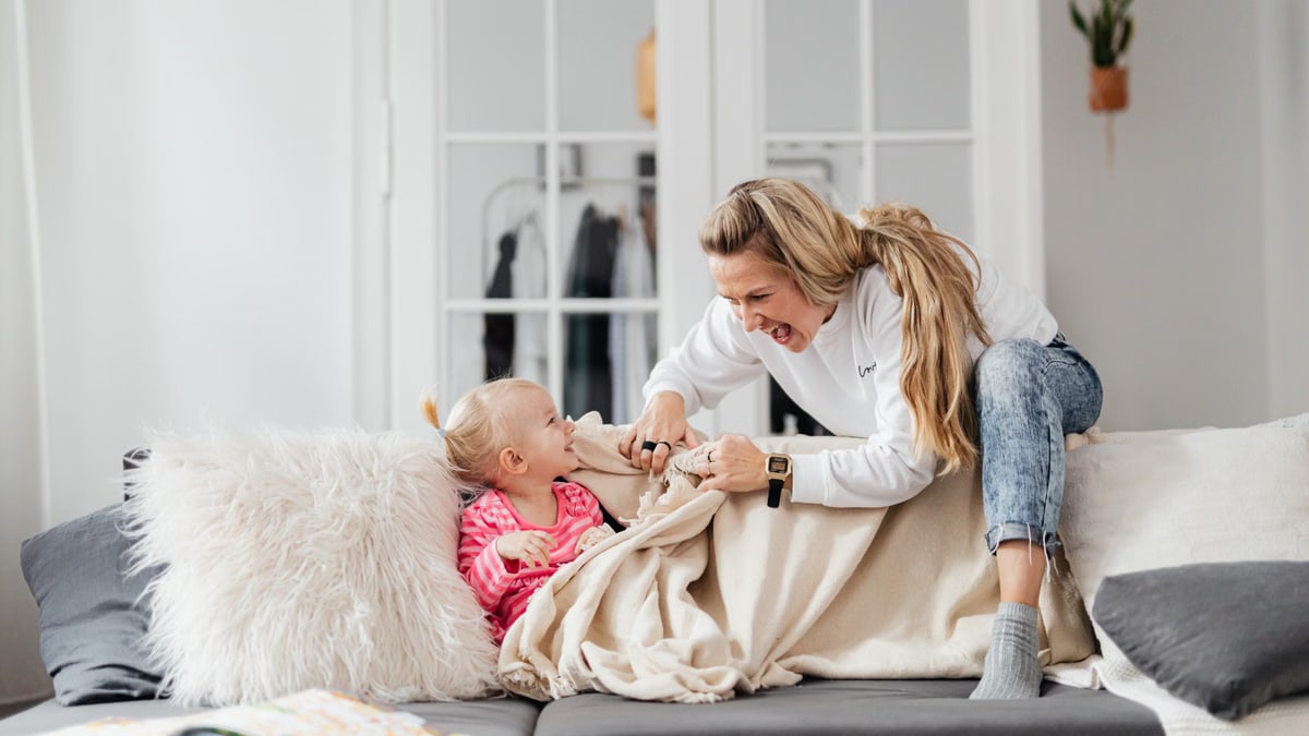 A joyful mother and daughter playing on a couch, embodying warmth and togetherness indoors.